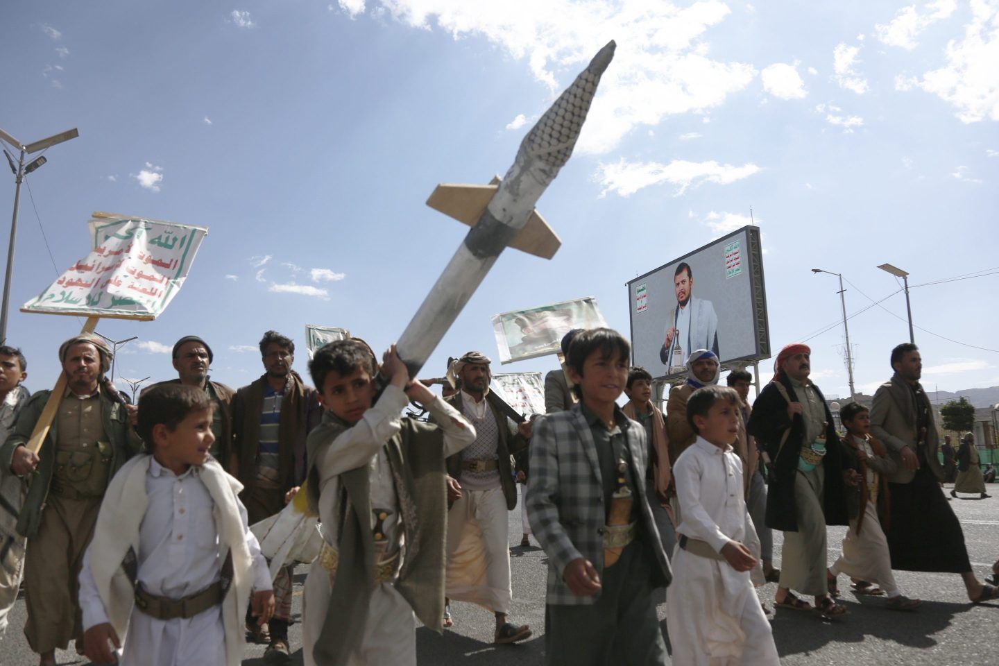 Yemeni children, one of them carrying a mock missile, walk next to a billboard depicting the Houthi leader Abdul Malik Al-Houthi to partake in a demonstration staged against the United States' aerial attacks on the capital Sana'a, and other provinces on March 17, 2025 in Sana'a, Yemen