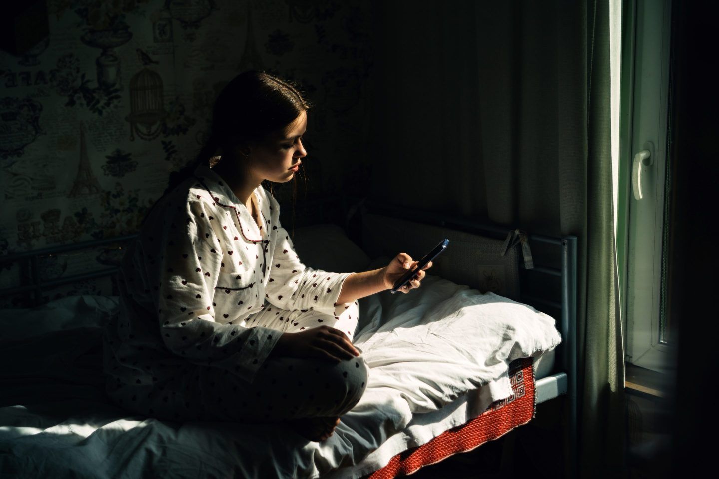 Teen girl using smartphone on her bed in the dark