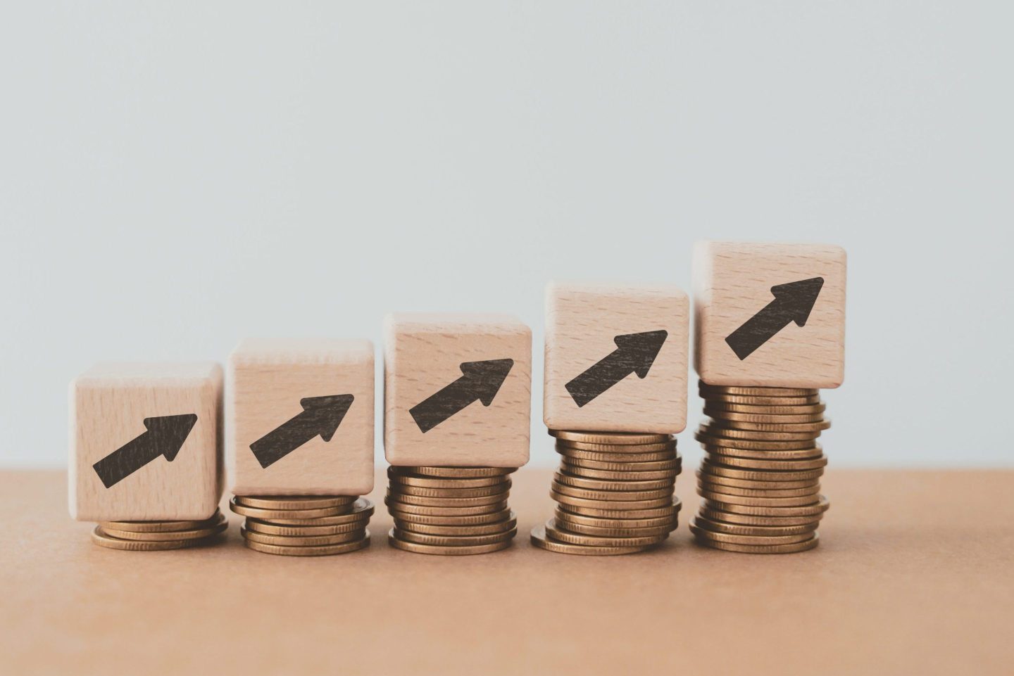 For financial growth, interest rate increase, inflation, high price and tax rise concept. Arrow up sign on wooden cube blocks above stack of coins including copy space