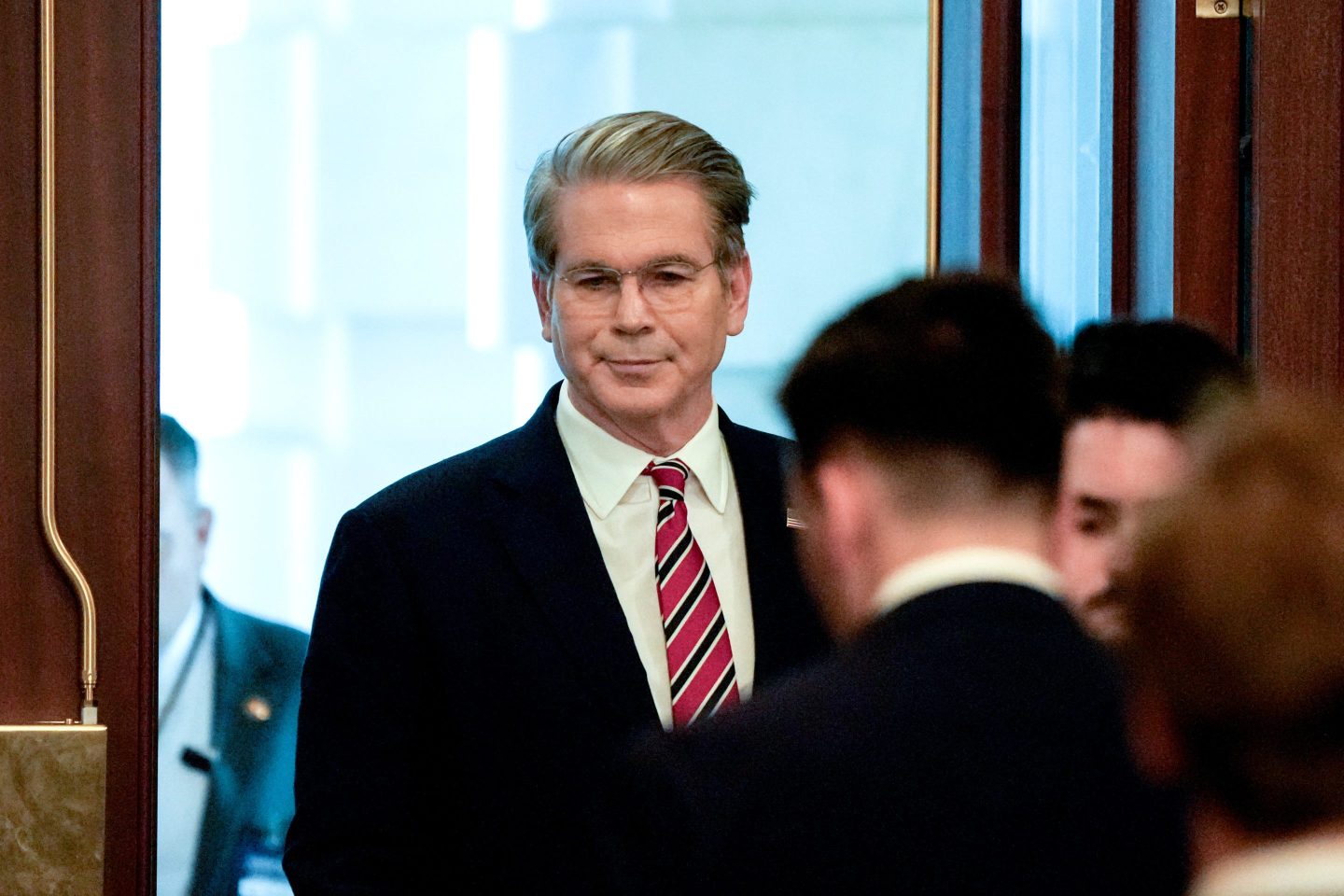 Treasury Secretary Scott Bessent, dressed in a suit and red- and black-striped tie, walks through a door in the U.S. capital.