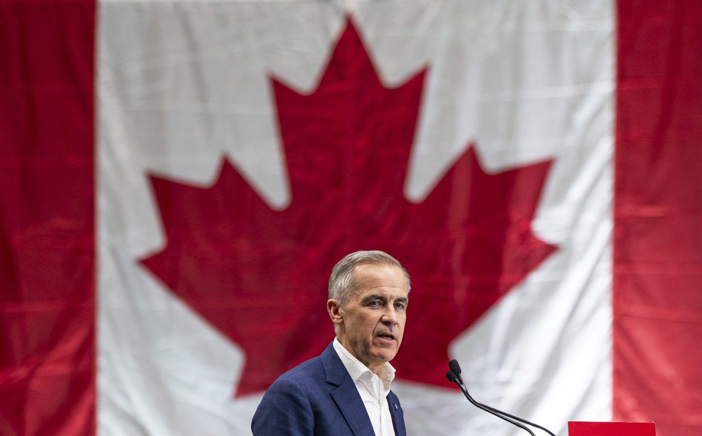 Mark Carney stands in front of a giant Canadian flag