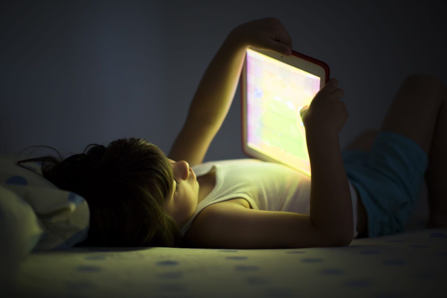 A child lying down holding up a glowing tablet