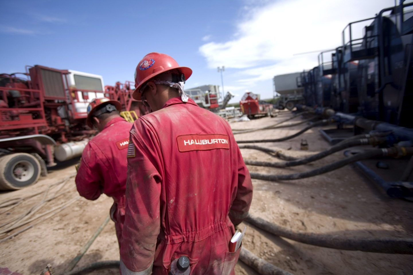 Two Halliburton employees, clad in red coveralls, work at a pressure pumping, or fracking, operation in the Permian Basin.