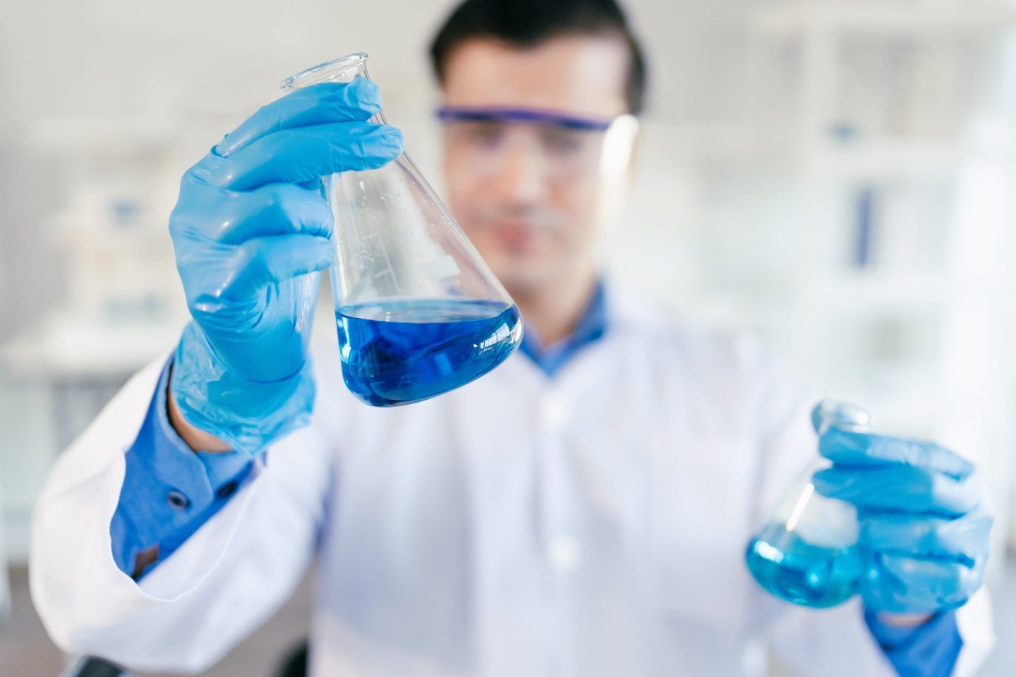 Man in white lab coat holding beaker of blue liquid