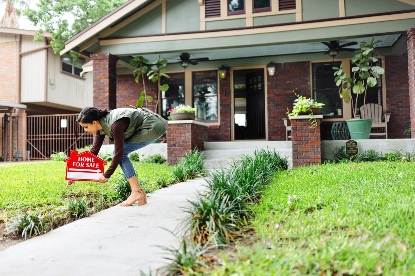 woman planting for-sale sign in front of her house