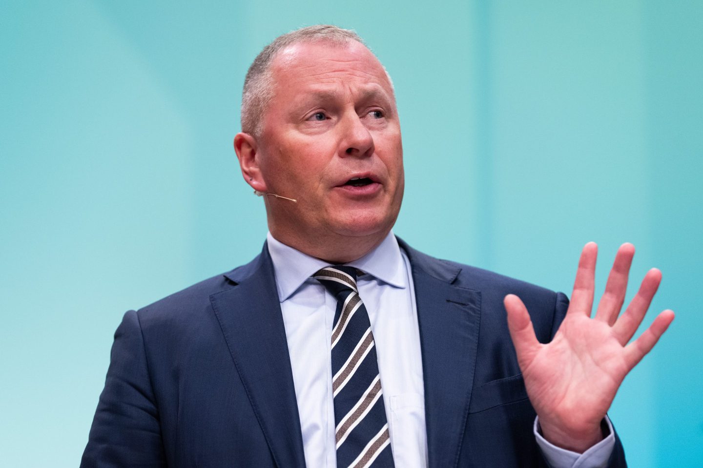 Norway Wealth Fund CEO Nicolai Tangen, wearing a suits, gestures with his left hand in front of a light blue background.