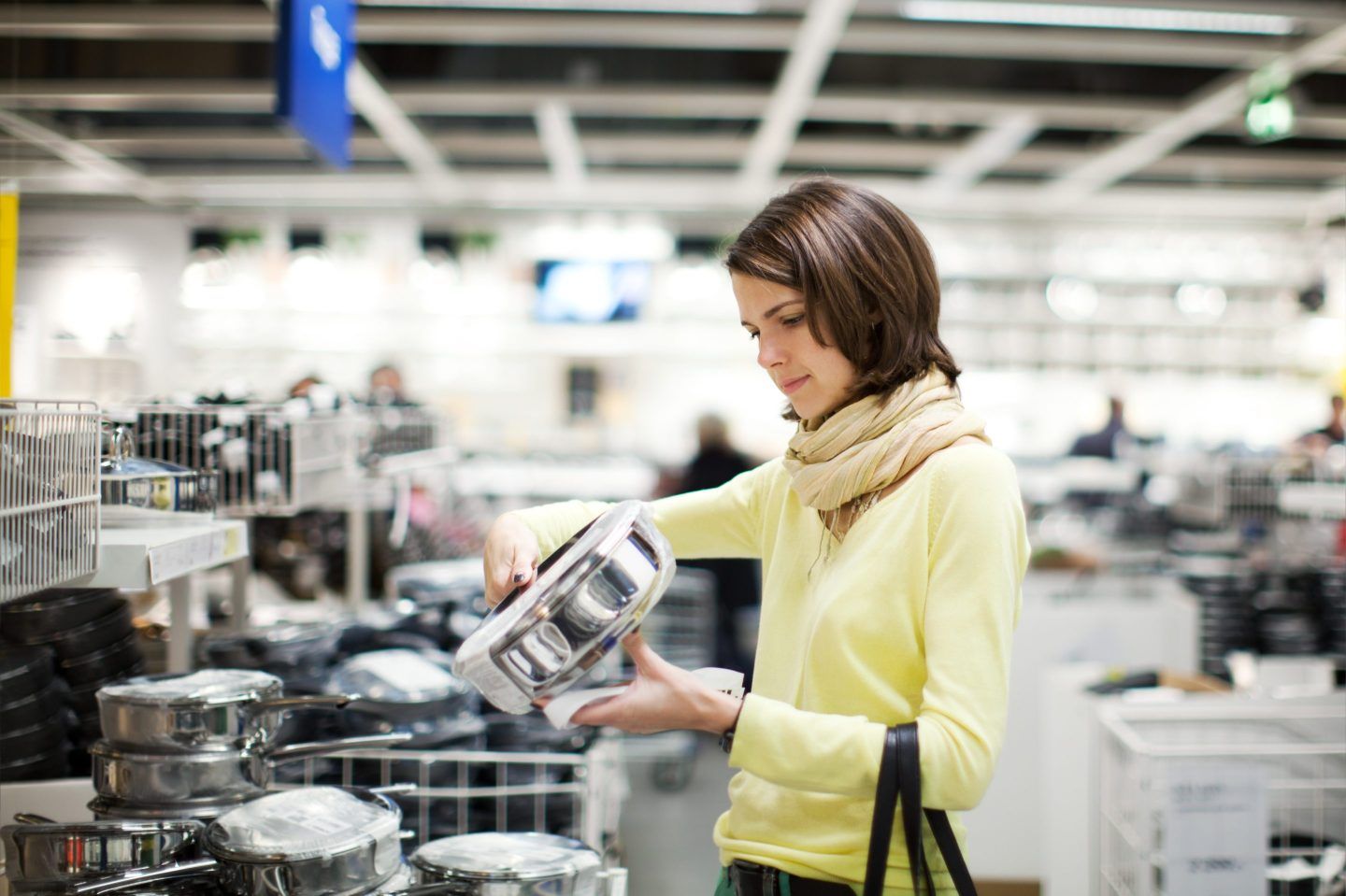A woman picks up and looks at a steel pot in a store.