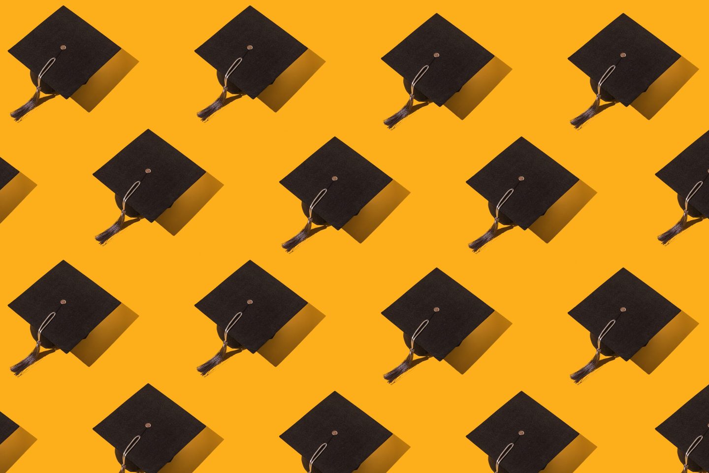 Pattern of black graduation caps with gray tassel with hard shadow on yellow background. Graduation, achievement, goal, degree, master, bachelor, university, college and success concept.