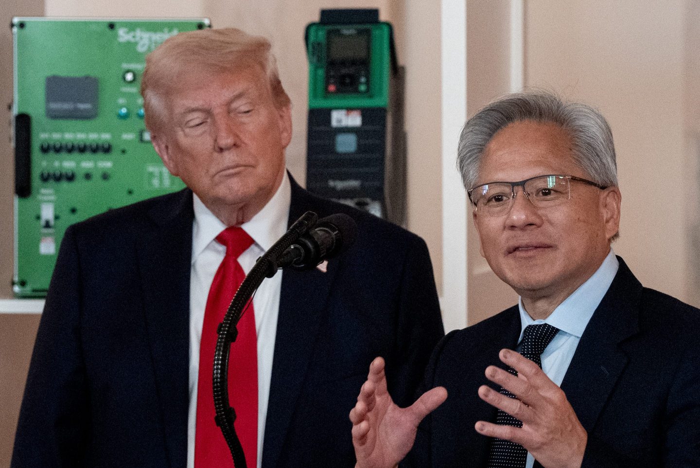 Donald Trump looks on at Jensen Huang, who is speaking in front of a podium.