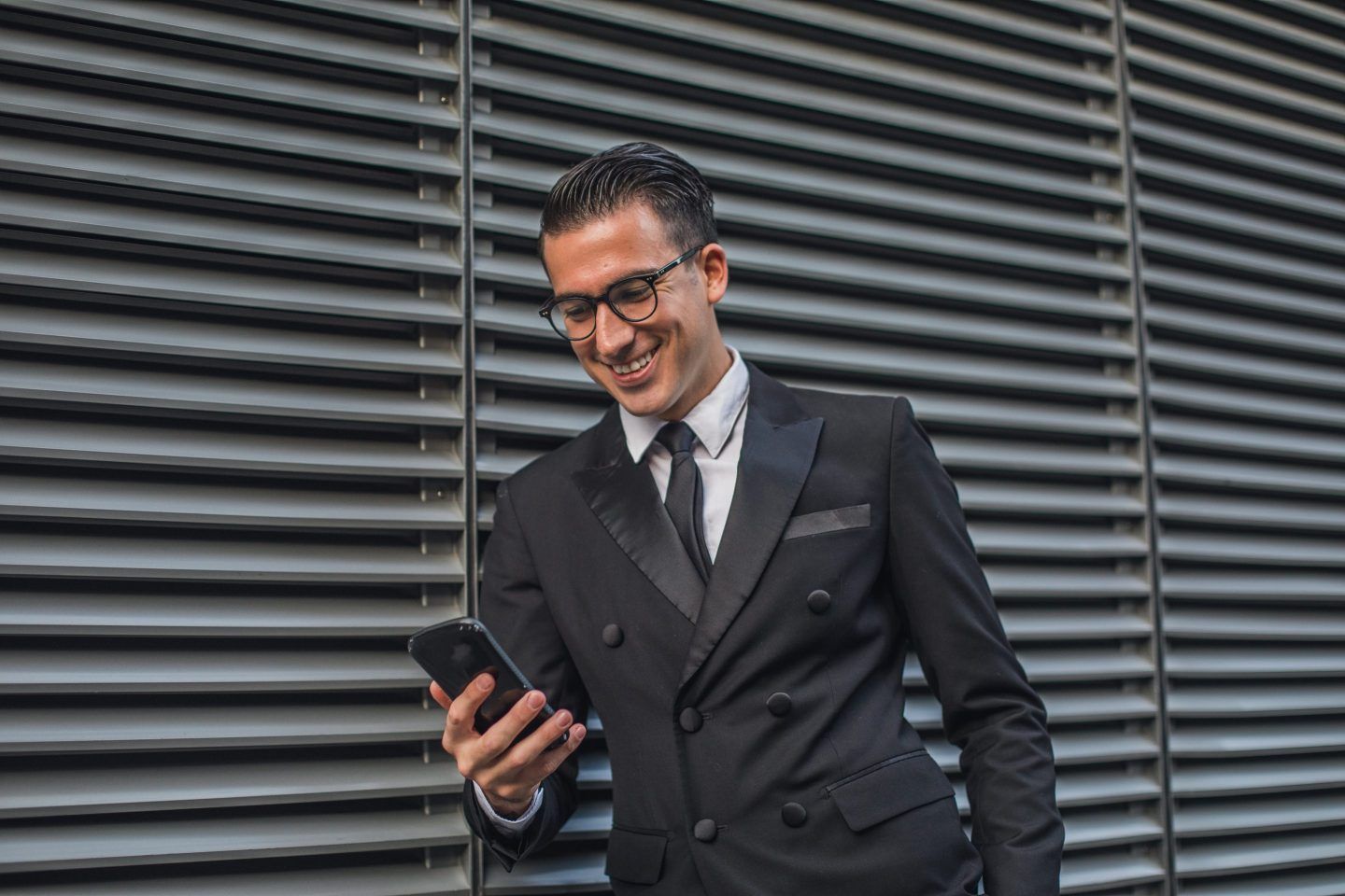 Business man stands outside looking down at this phone.