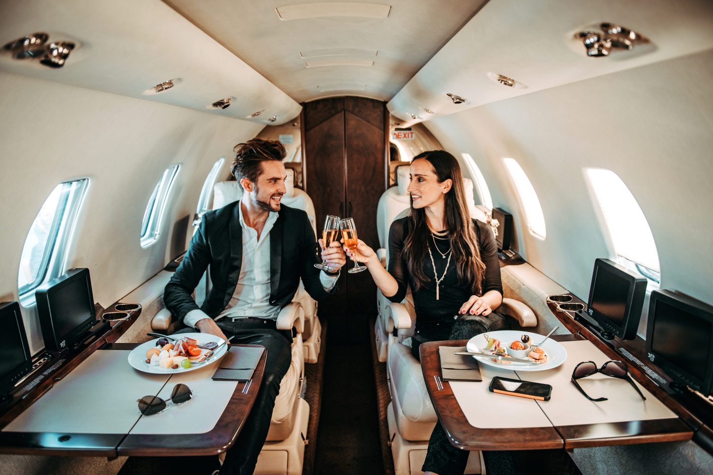 Rich couple making a toast with champagne glasses while eating aboard a private jet.