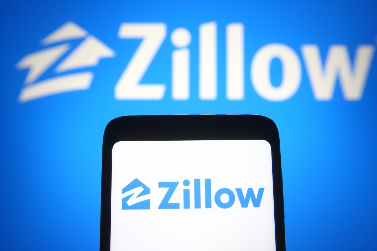 The Zillow logo on a phone, in front of a blue Zillow logo background