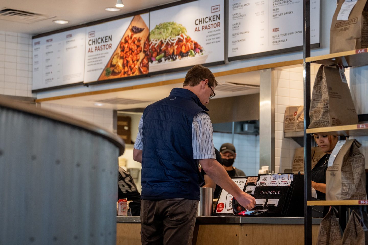 A man in a vest pays at the Chipotle counter.