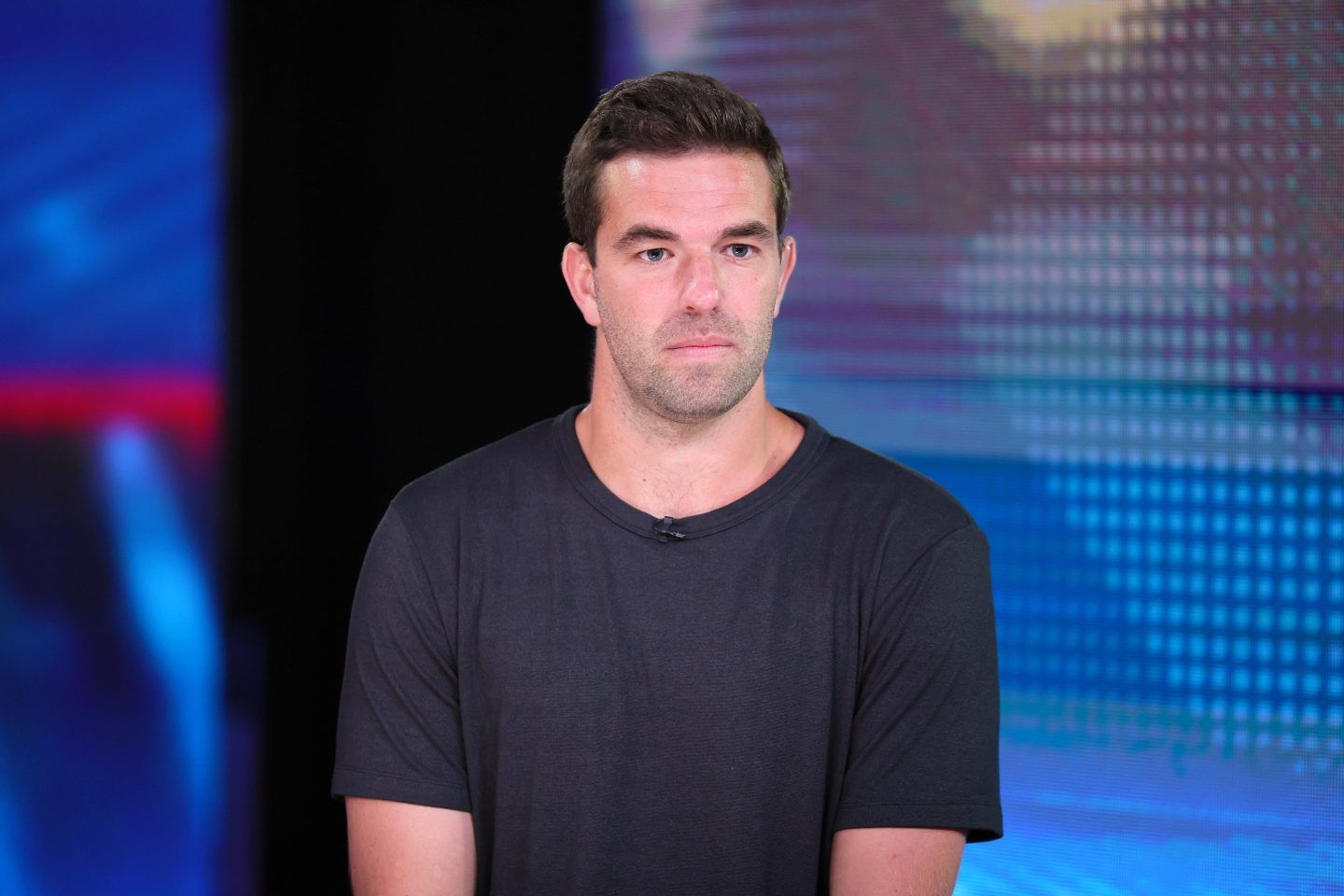 Billy McFarland, sitting in front of a lit blue background, looks forward and frowns.