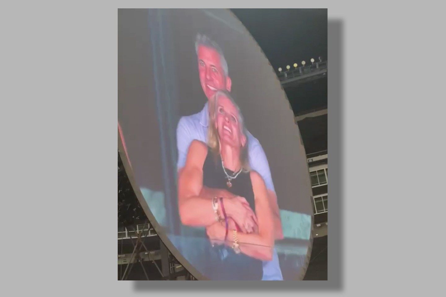 A man on a jumbotron hugging a woman from behind.