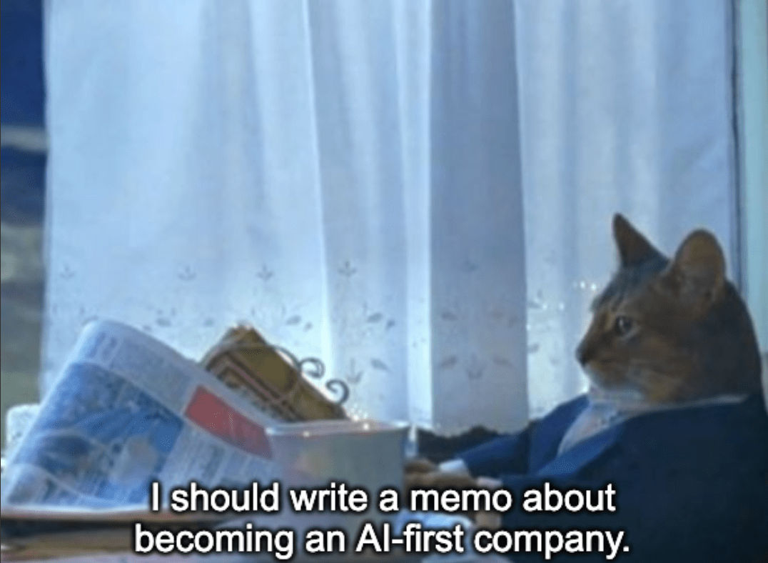 A meme featuring a still of an anthropomorphized cat wearing a suit and reading a newspaper with the caption, "I should write a memo about becoming an AI-first company."