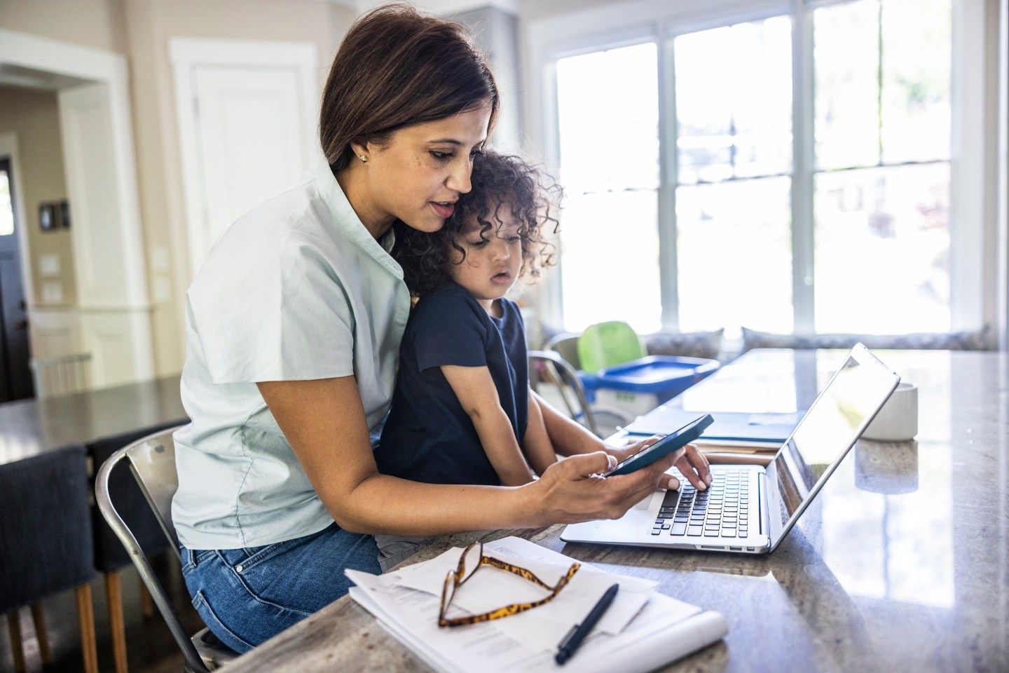 Mother working from home while holding toddler boy