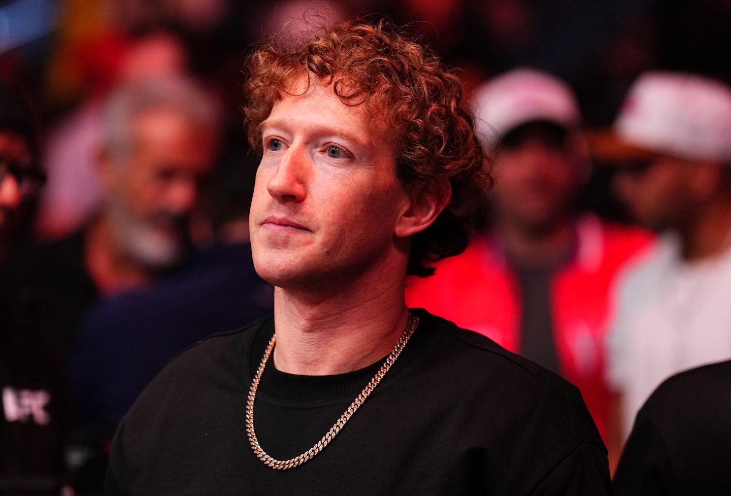 Mark Zuckerberg, wearing a black shirt and chain, looks to his right.