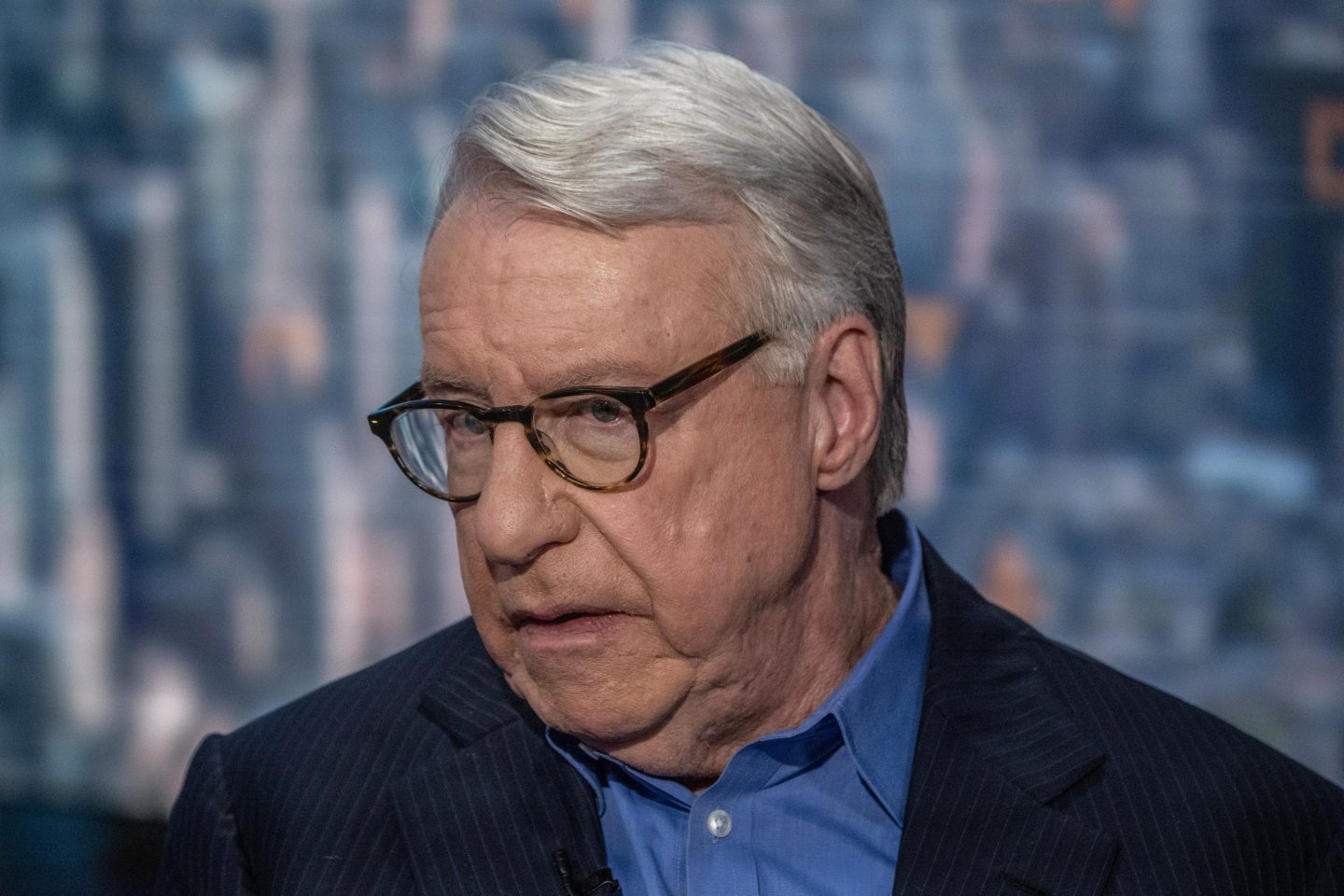 Jim Chanos, wearing a blue shirt and dark suit, looks off to the side, brows furrowed.