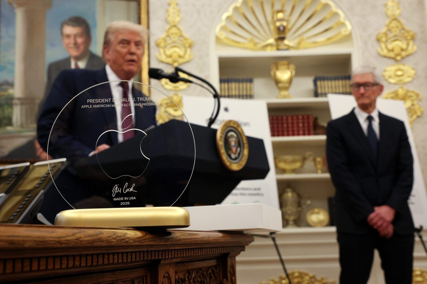 Donald Trump and Tim Cook in the Oval Office standing behind a glass plaque resting on a desk