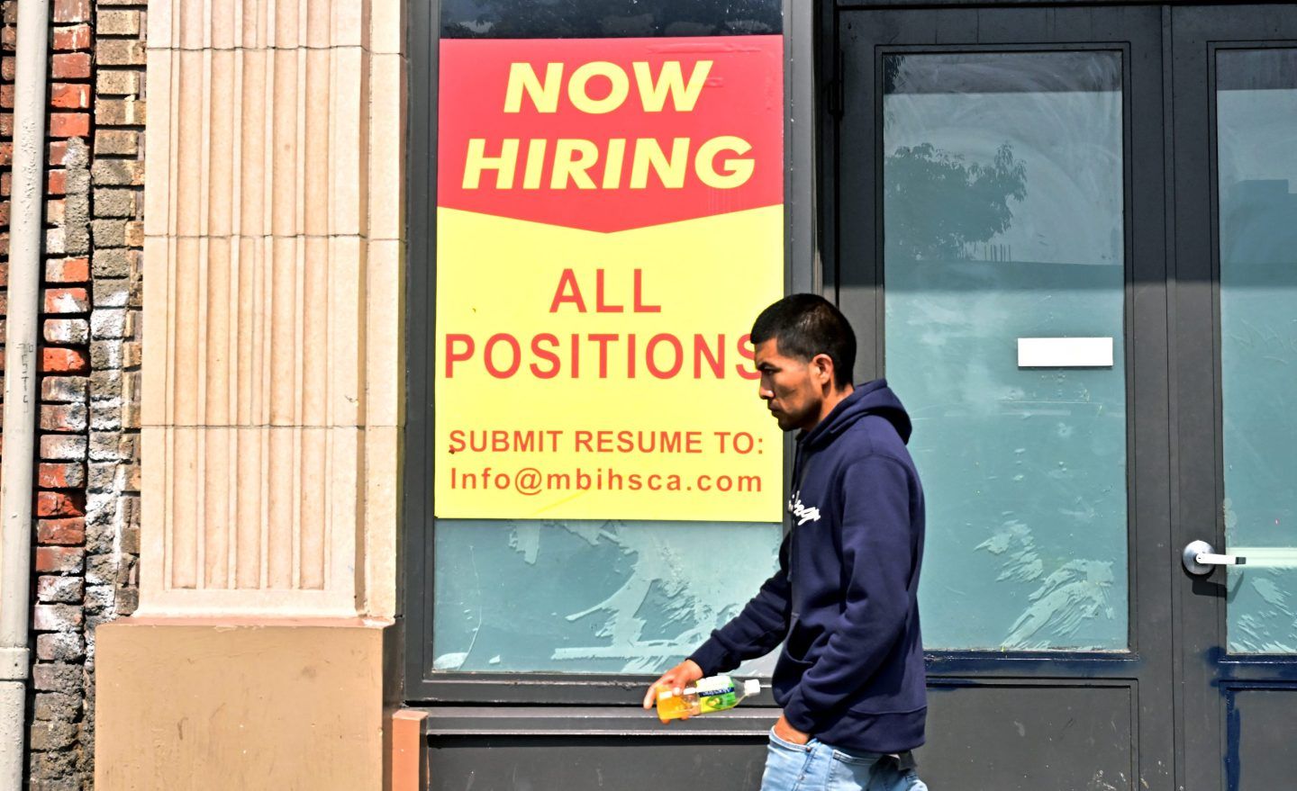 Guy walks by a sign that says "now hiring."