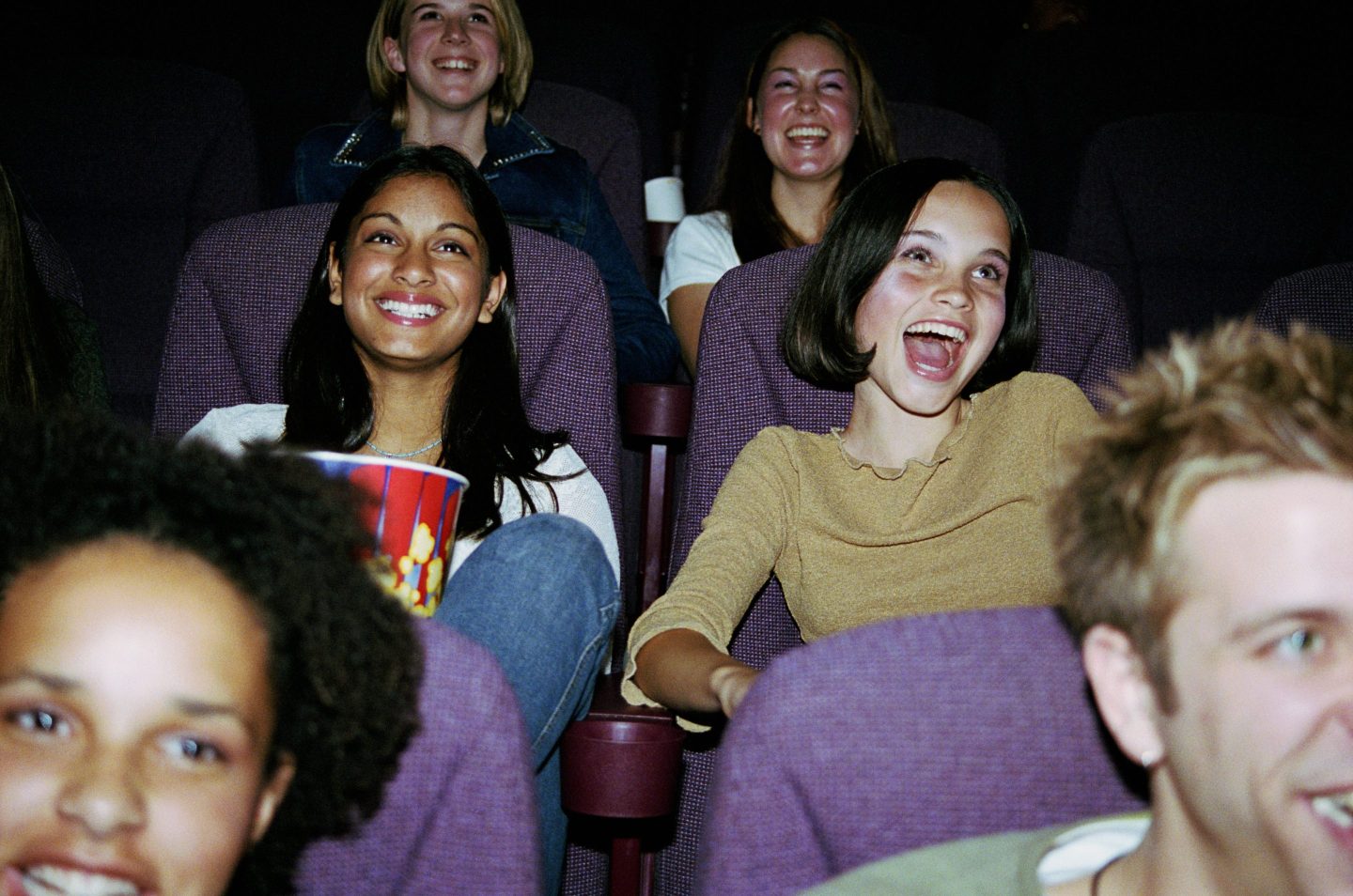 Teenage girls laugh at the movies.