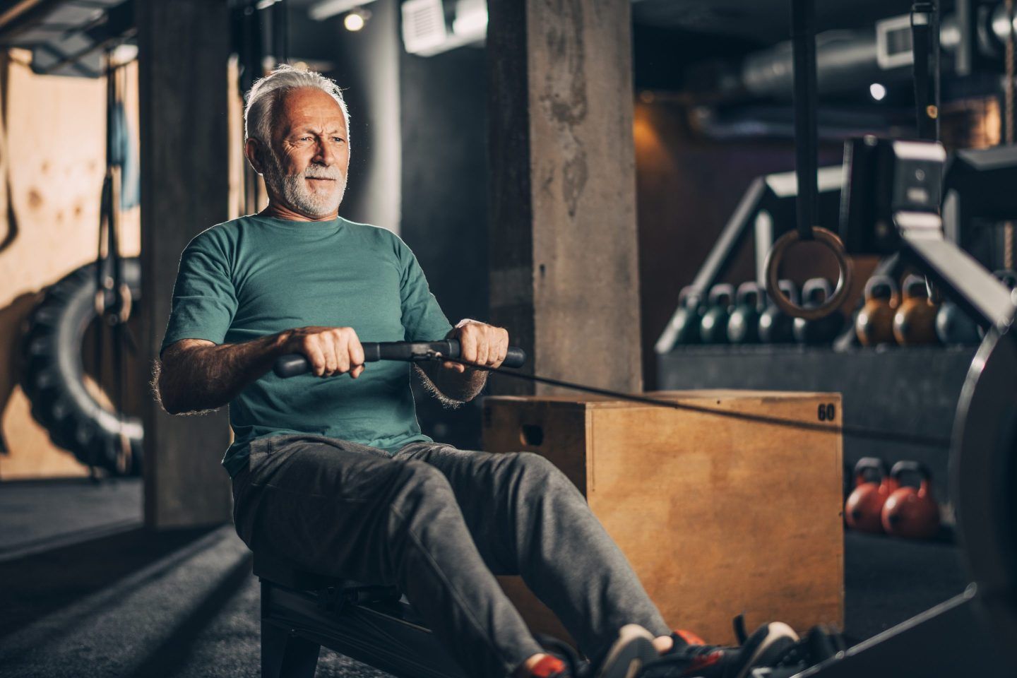 A happy old man wearing a green shirt smiles on a rowing machine
