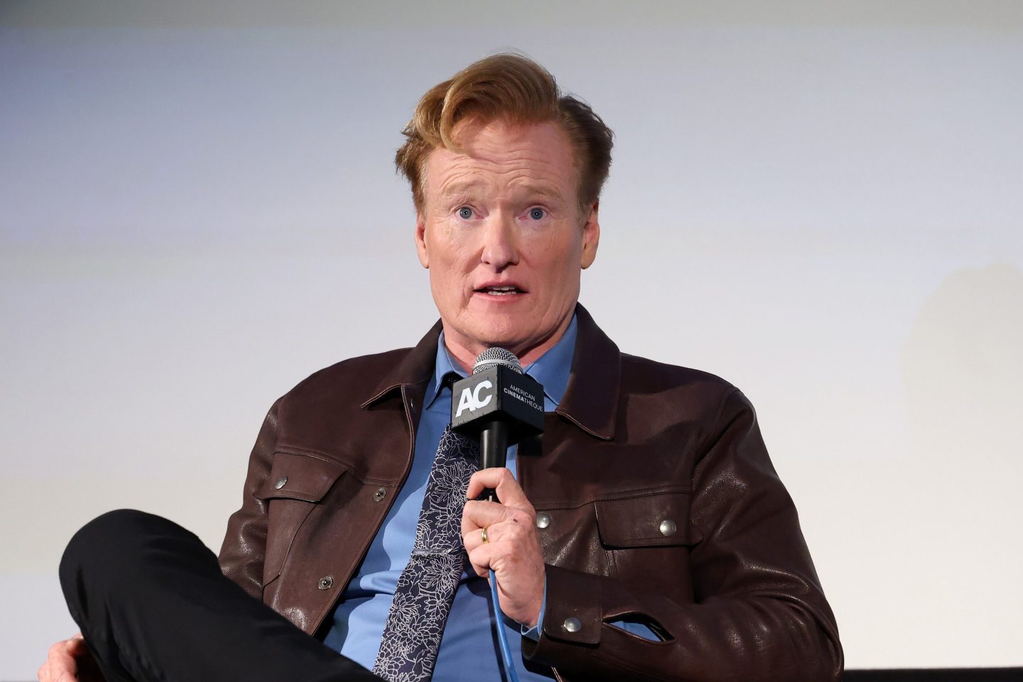 Conan O'Brien sits, speaking into a microphone