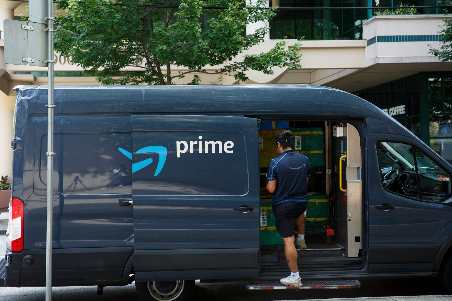 Amazon delivery worker steps up into a blue delivery van with Prime logo