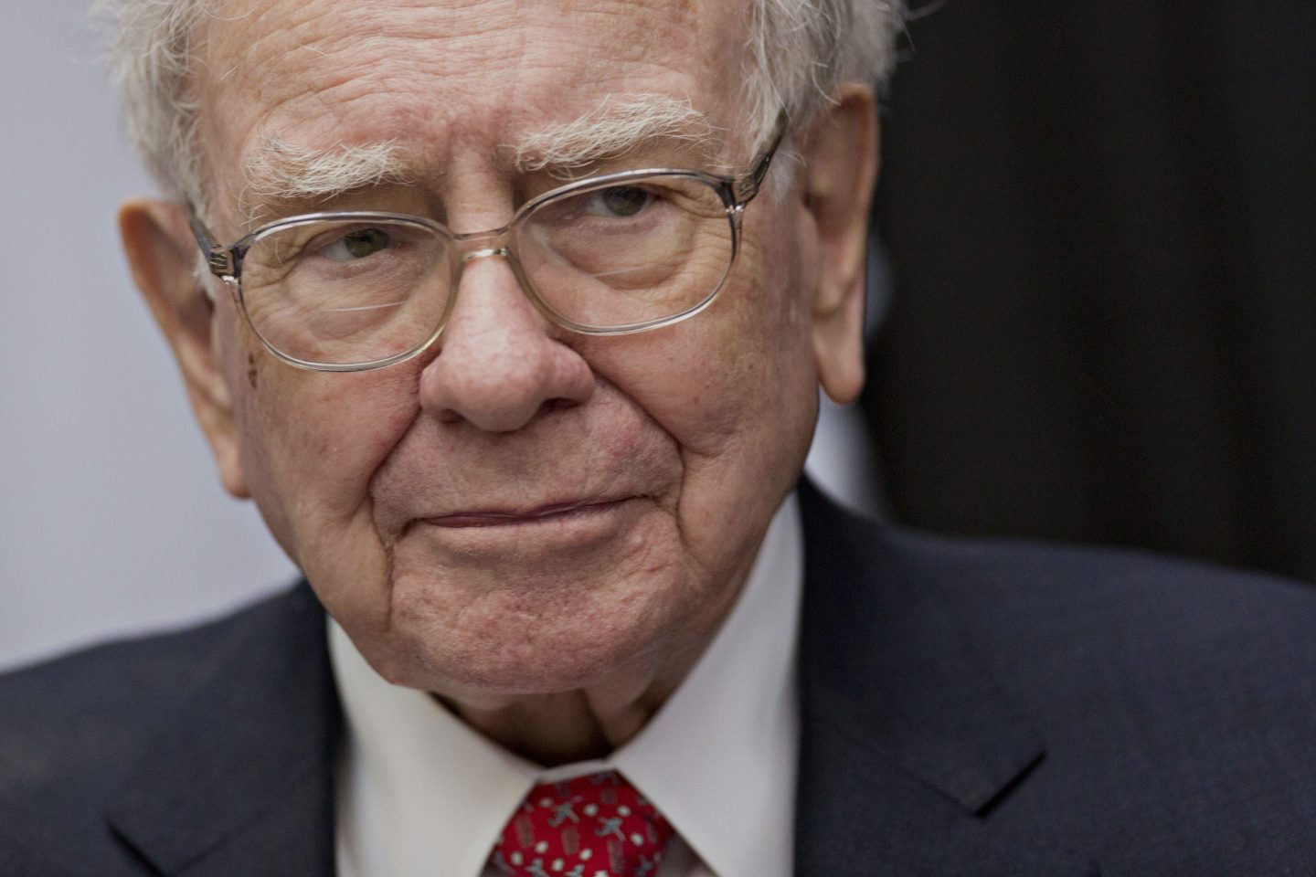Warren Buffet, in glasses and a red tie, looks to the side of the camera.