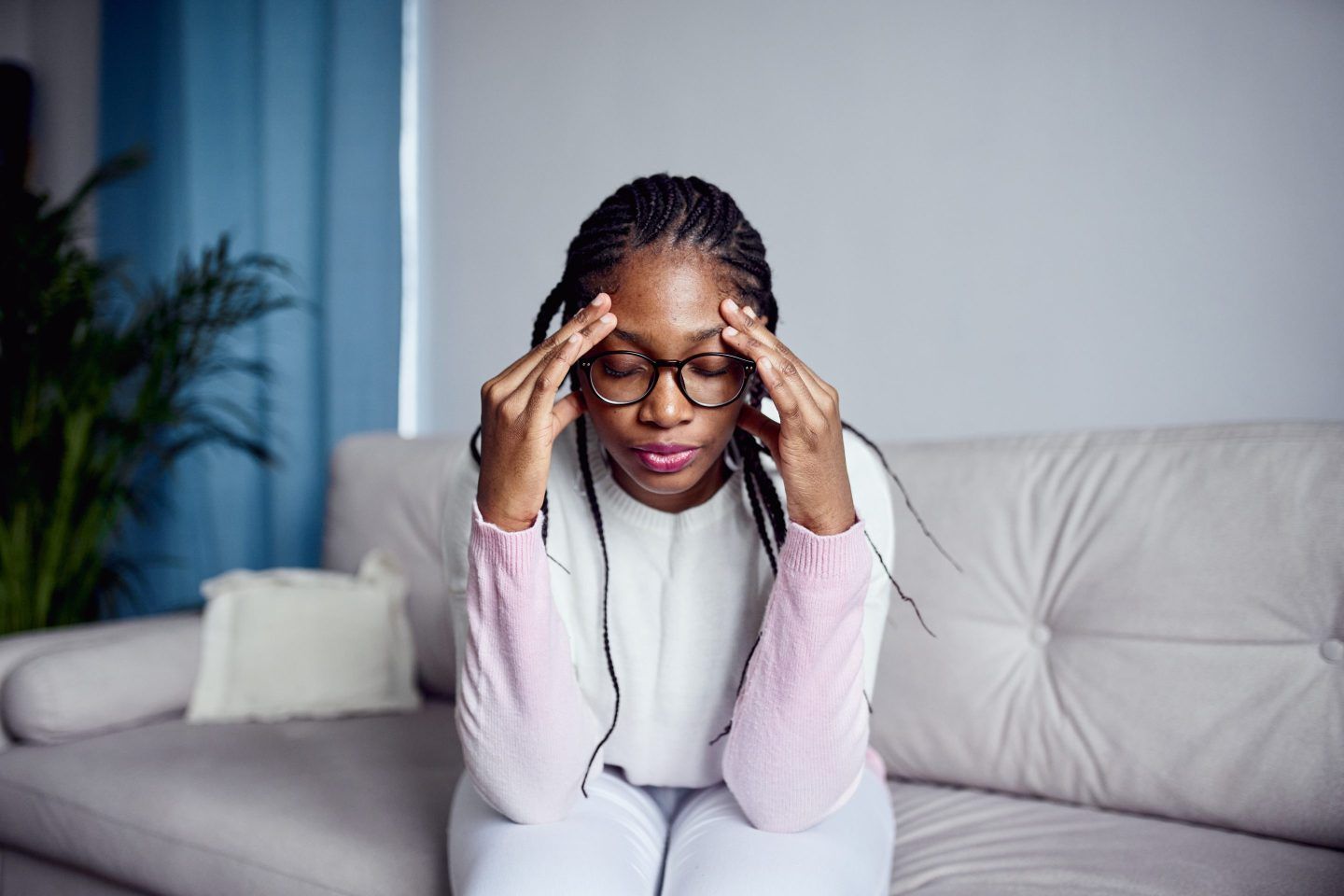 A young woman is sitting on the sofa at home with her head in her hands.