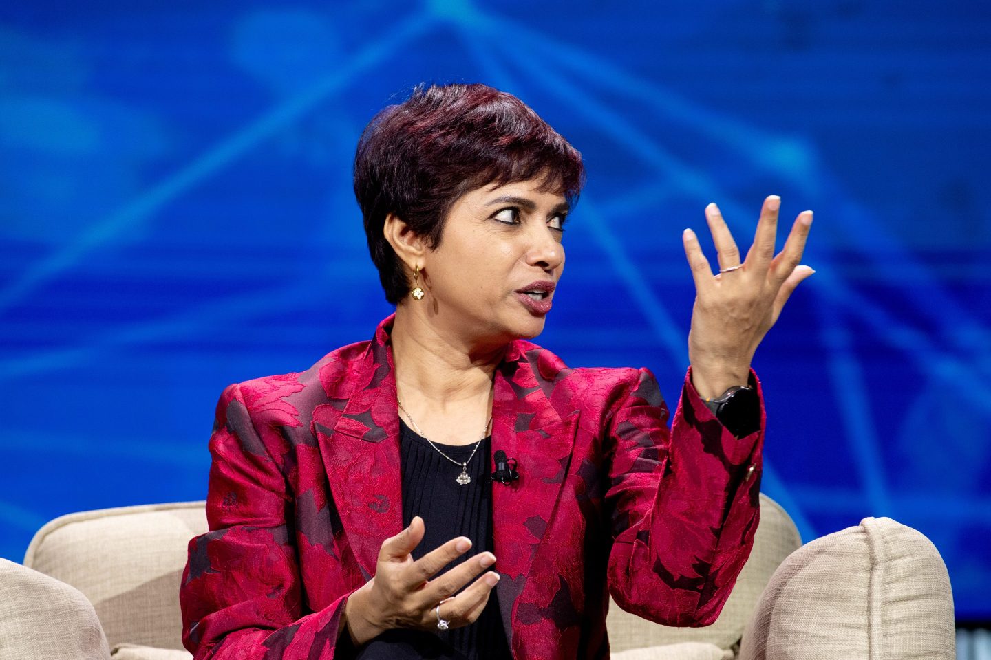 Jyoti Deshpande, wearing a burgundy jacket, speaks lifting on hand in the air while gesturing with the other.