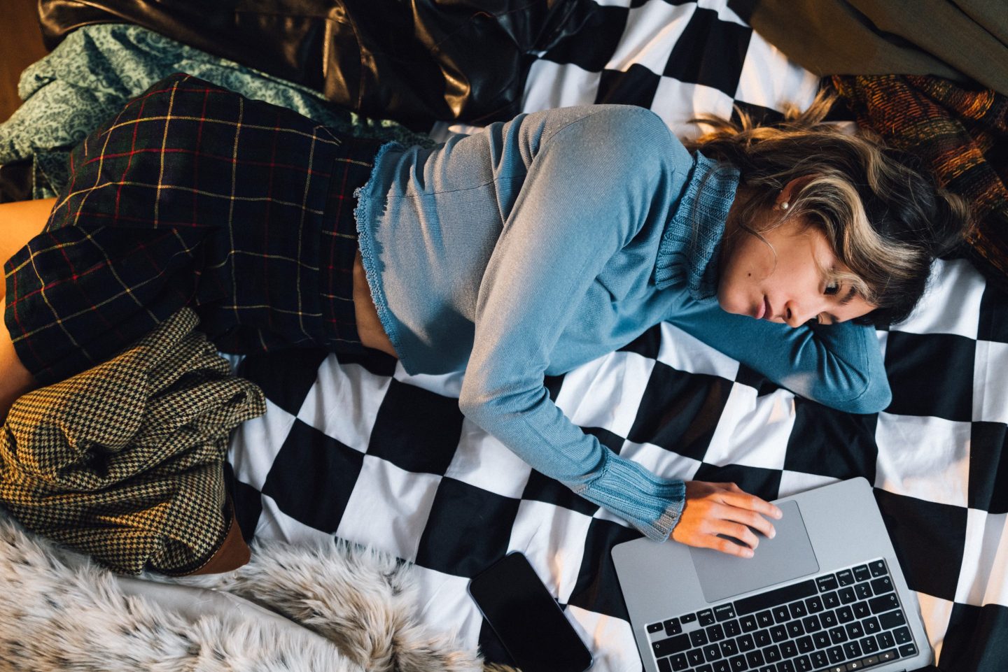 A young woman lies sideways, looking at her laptop and frowning.