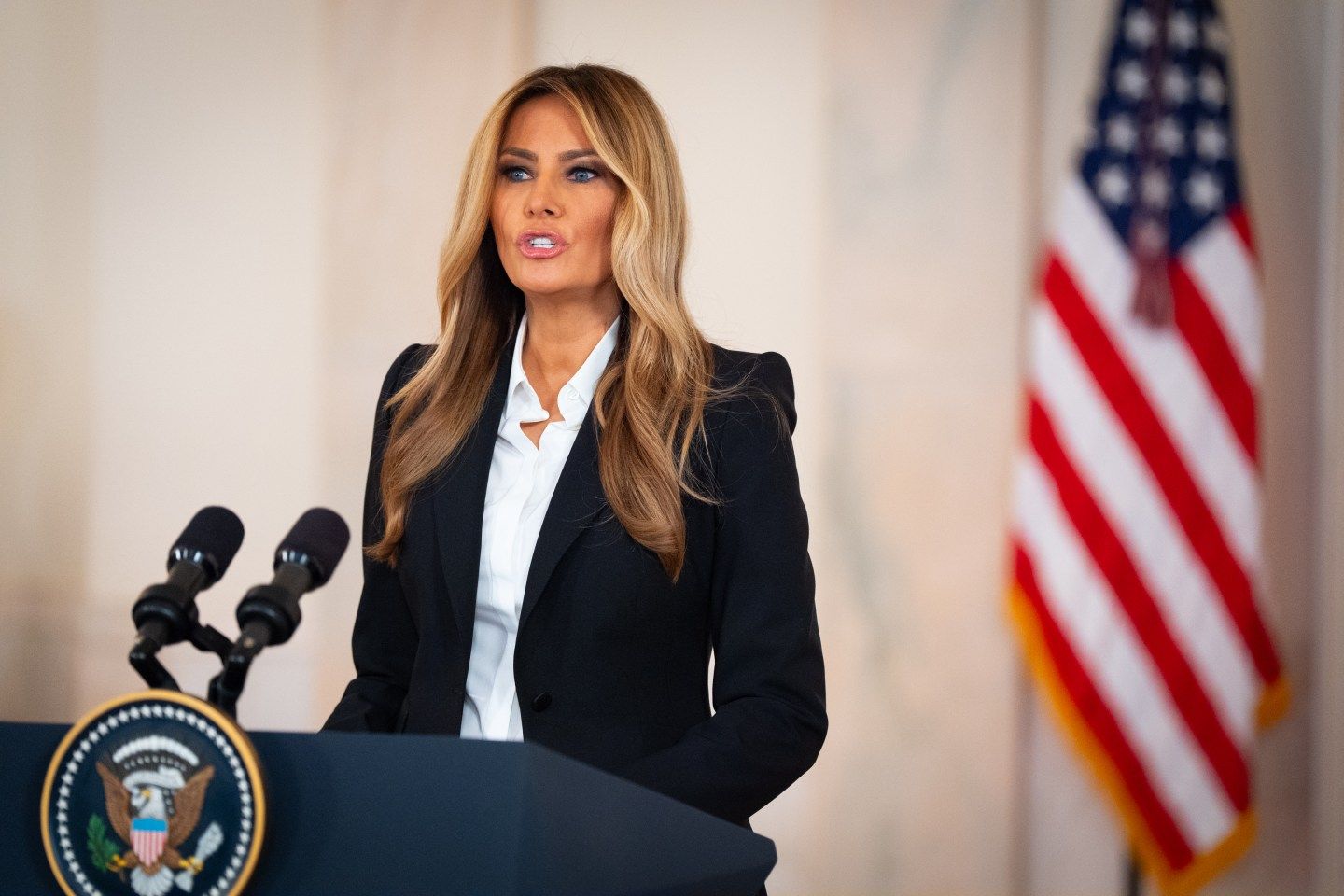 Melania Trump standing behind a podium with American flag behind her