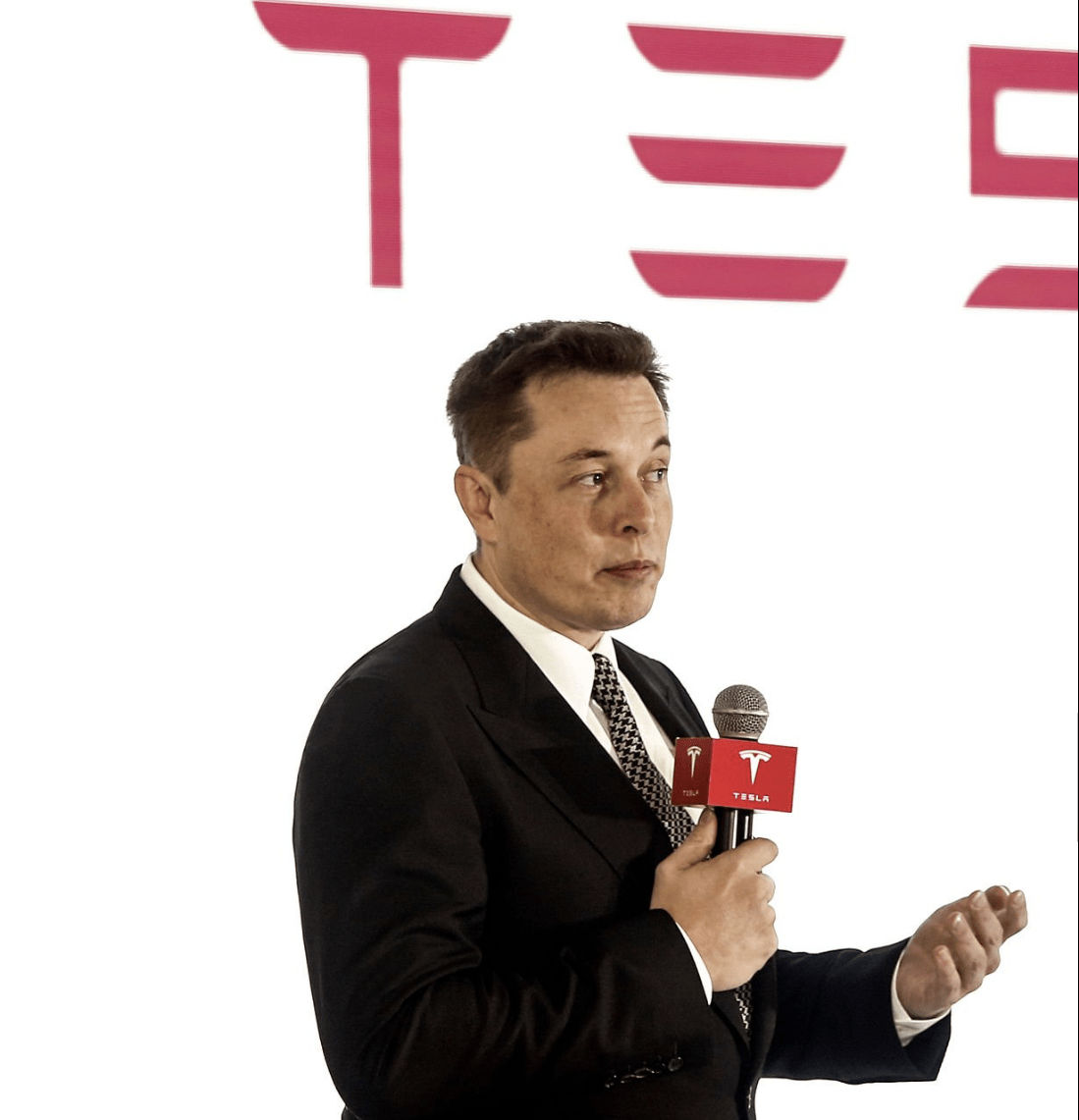 elon musk on stage in front of Tesla signage in red letters