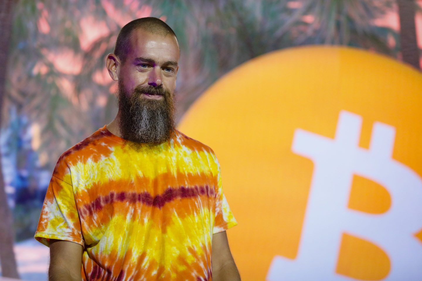Jack Dorsey stands on stage next to a Bitcoin logo.