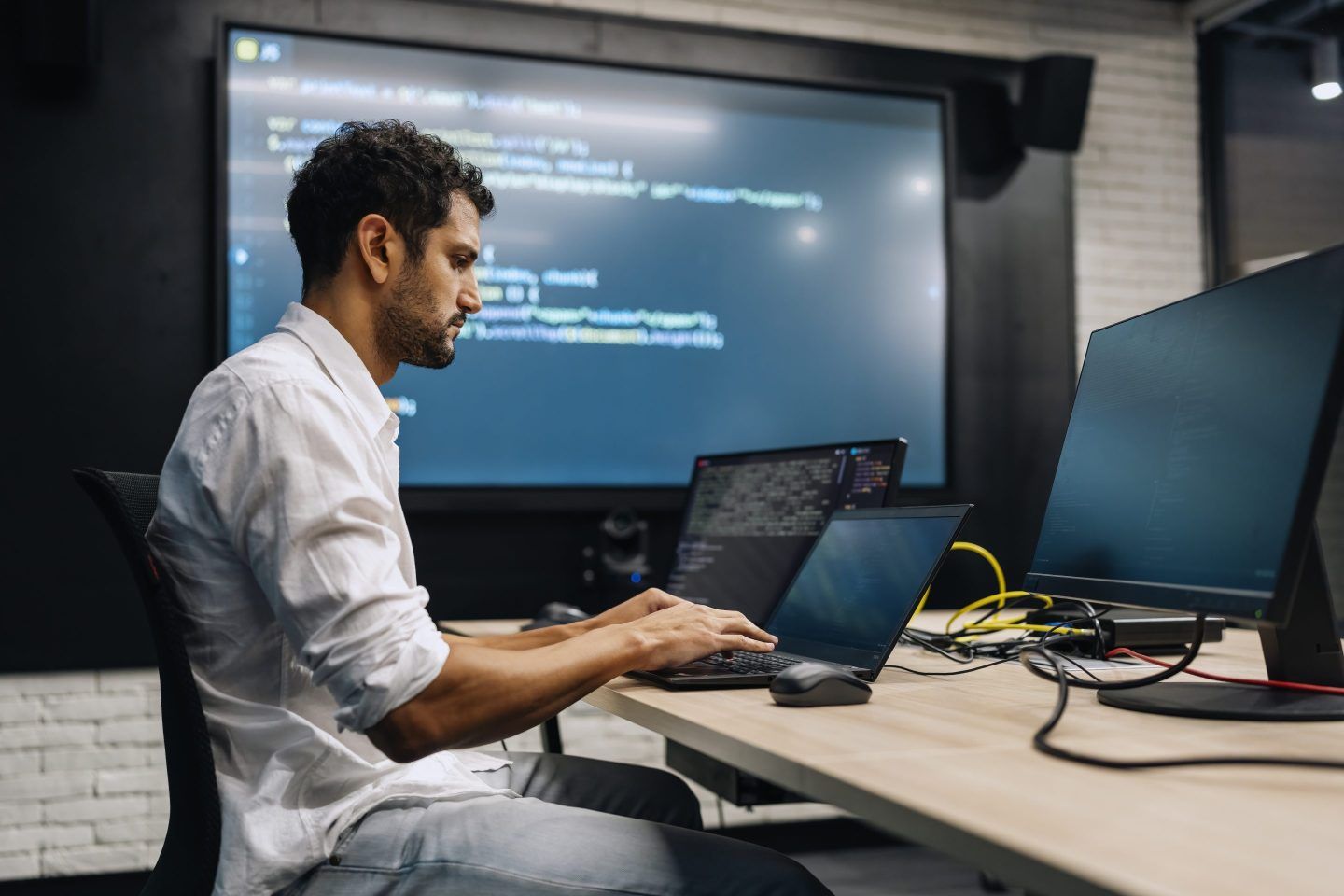 Professional software developer working late at night writing codes in an office. Mature computer programmer sitting in his office, using laptop and coding late at night.