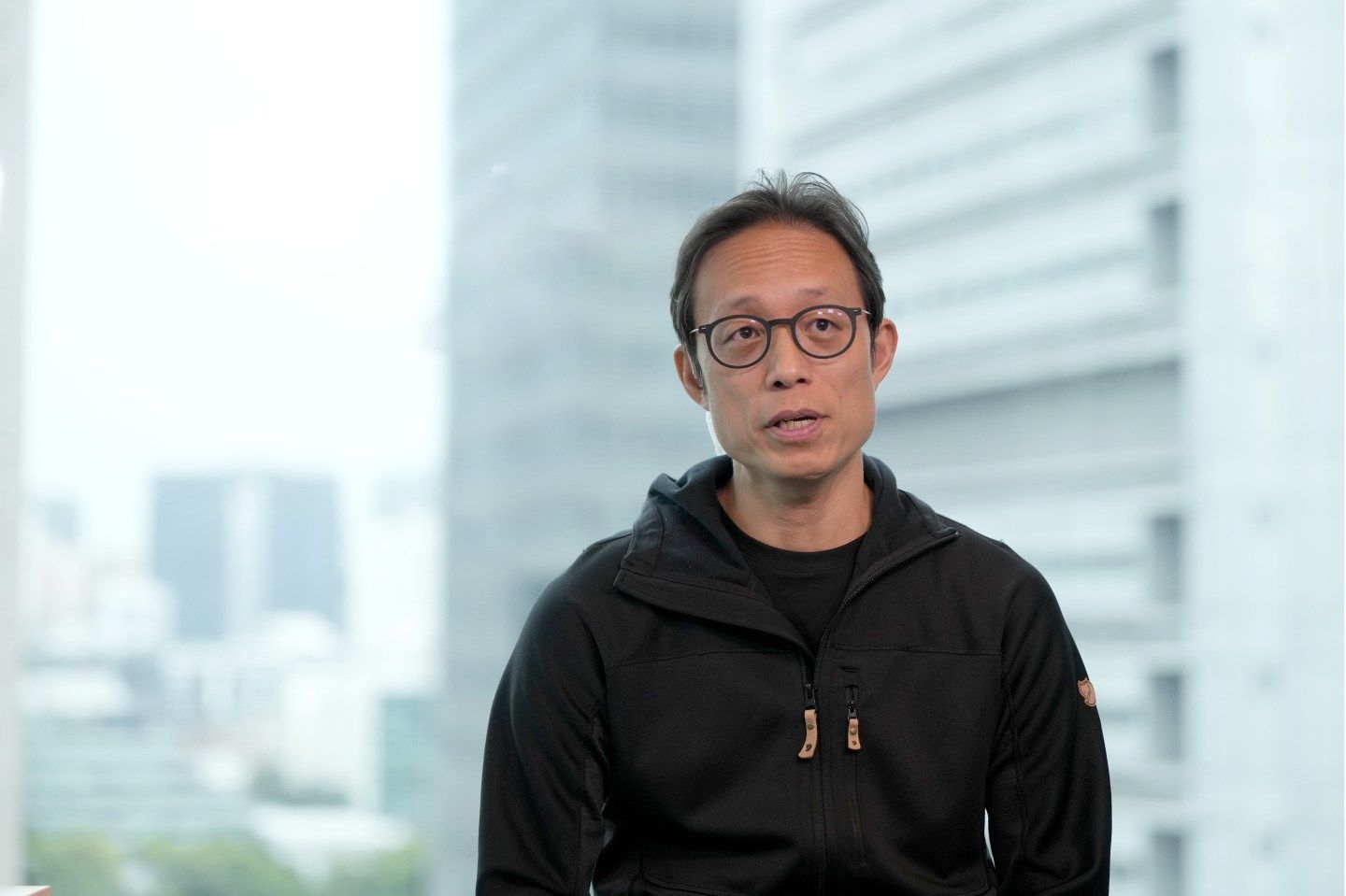 A man in a black hoodie and glasses is speaking