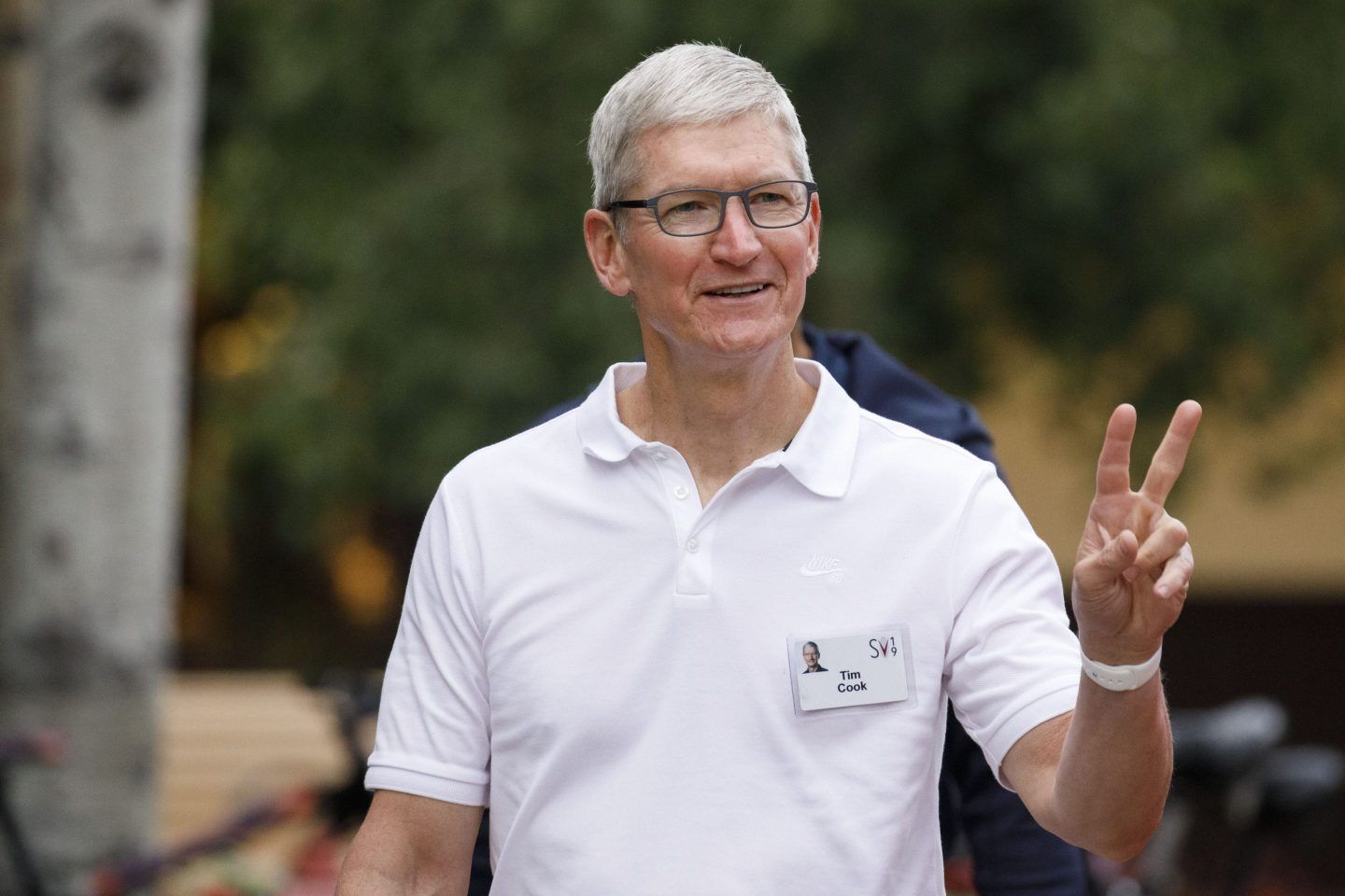 Apple CEO Tim Cook wearing a white polo shirt and throwing up a peace sign