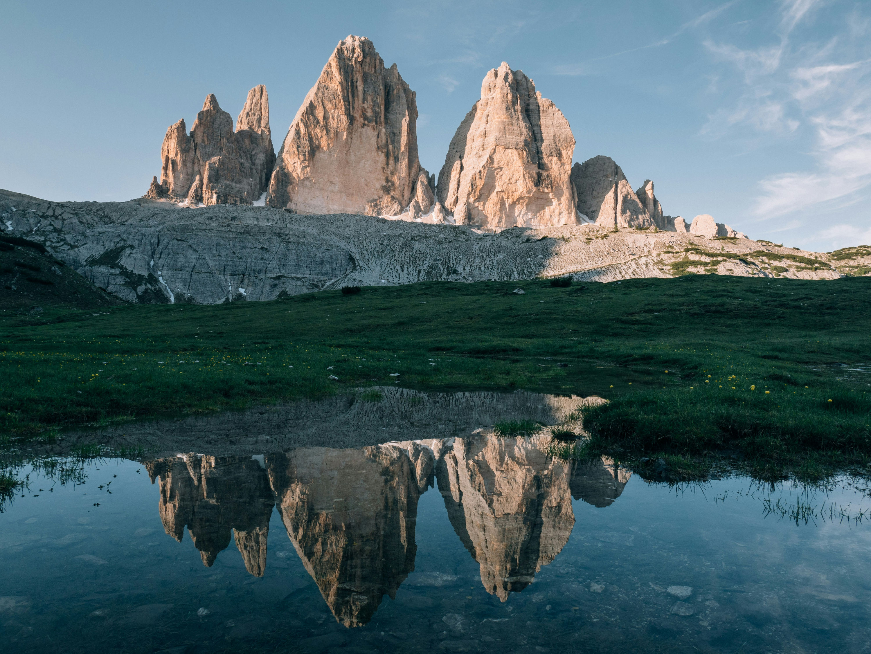 The Tre Cime di Lavaredo peaks reflected in a small alpine lake at sunset.