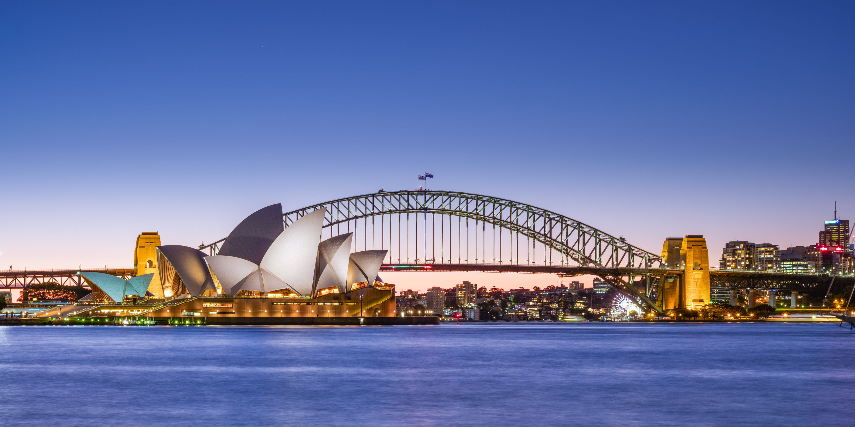 The Sydney Opera House and Harbour Bridge across the water at twilight.