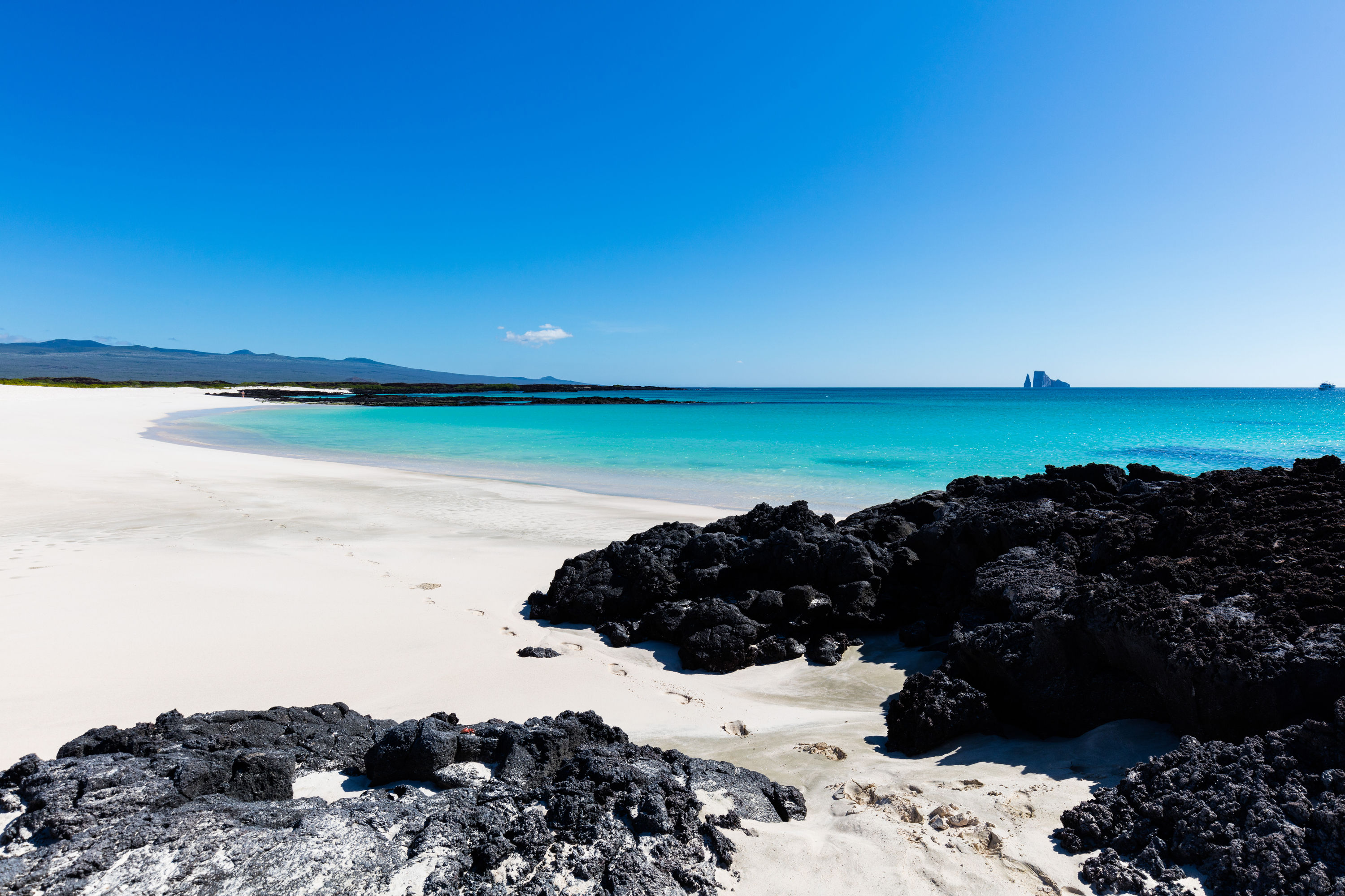 A white sand beach with turquoise water and Kicker Rock in the distance.