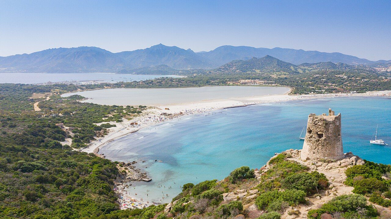 Aerial view of Porto Giunco beach, turquoise water, and a Spanish coastal tower.