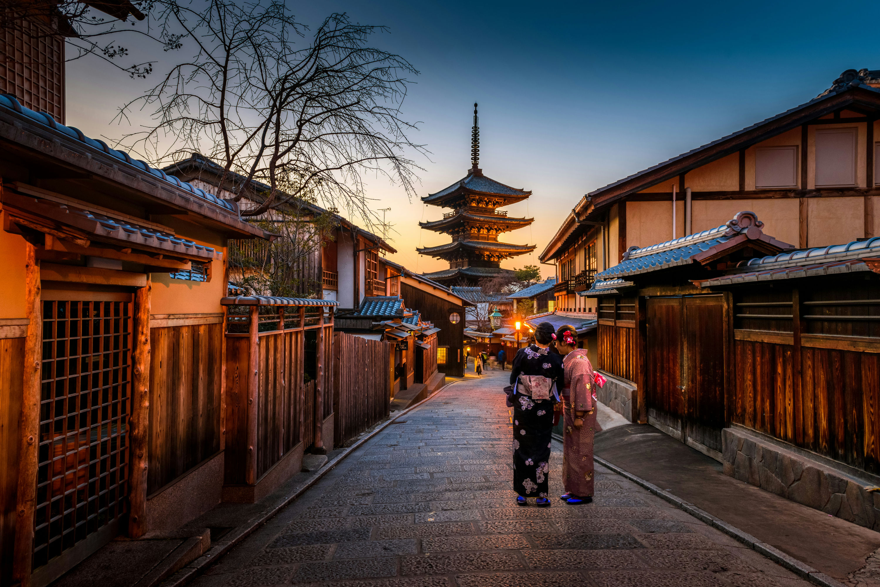 Two women in kimonos walking toward the Yasaka Pagoda at sunset in Kyoto.