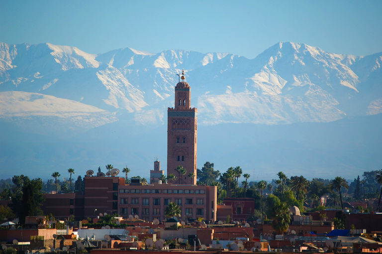 The Koutoubia minaret rising above the city rooftops with the snow-capped Atlas Mountains in the background.