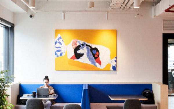 High ceiling office space with woman sitting in a private booth with blue cushions