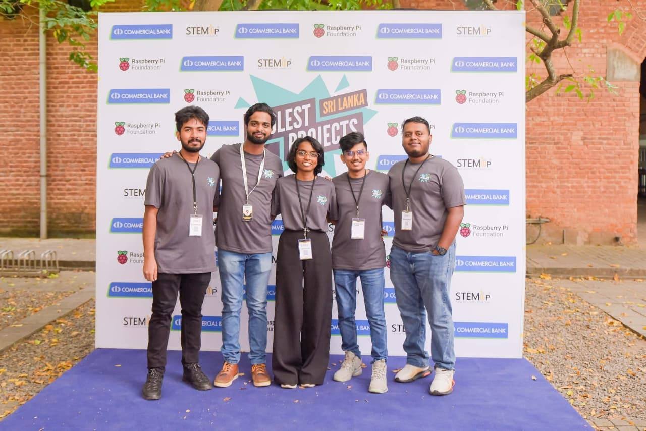 Aweesha Wijesundara with his marketing and creative team in matching grey T-shirts at the Coolest Projects Sri Lanka backdrop
