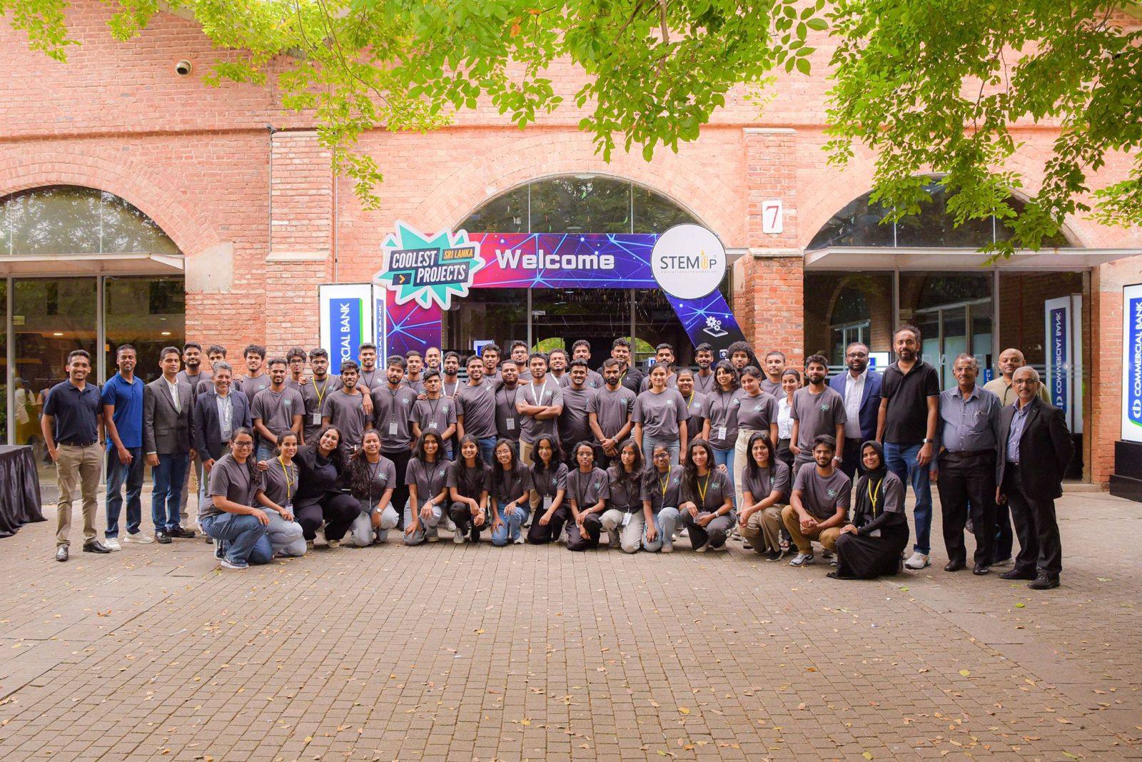 Aweesha Wijesundara with the full Coolest Projects Sri Lanka 2025 team in grey T-shirts outside the venue entrance