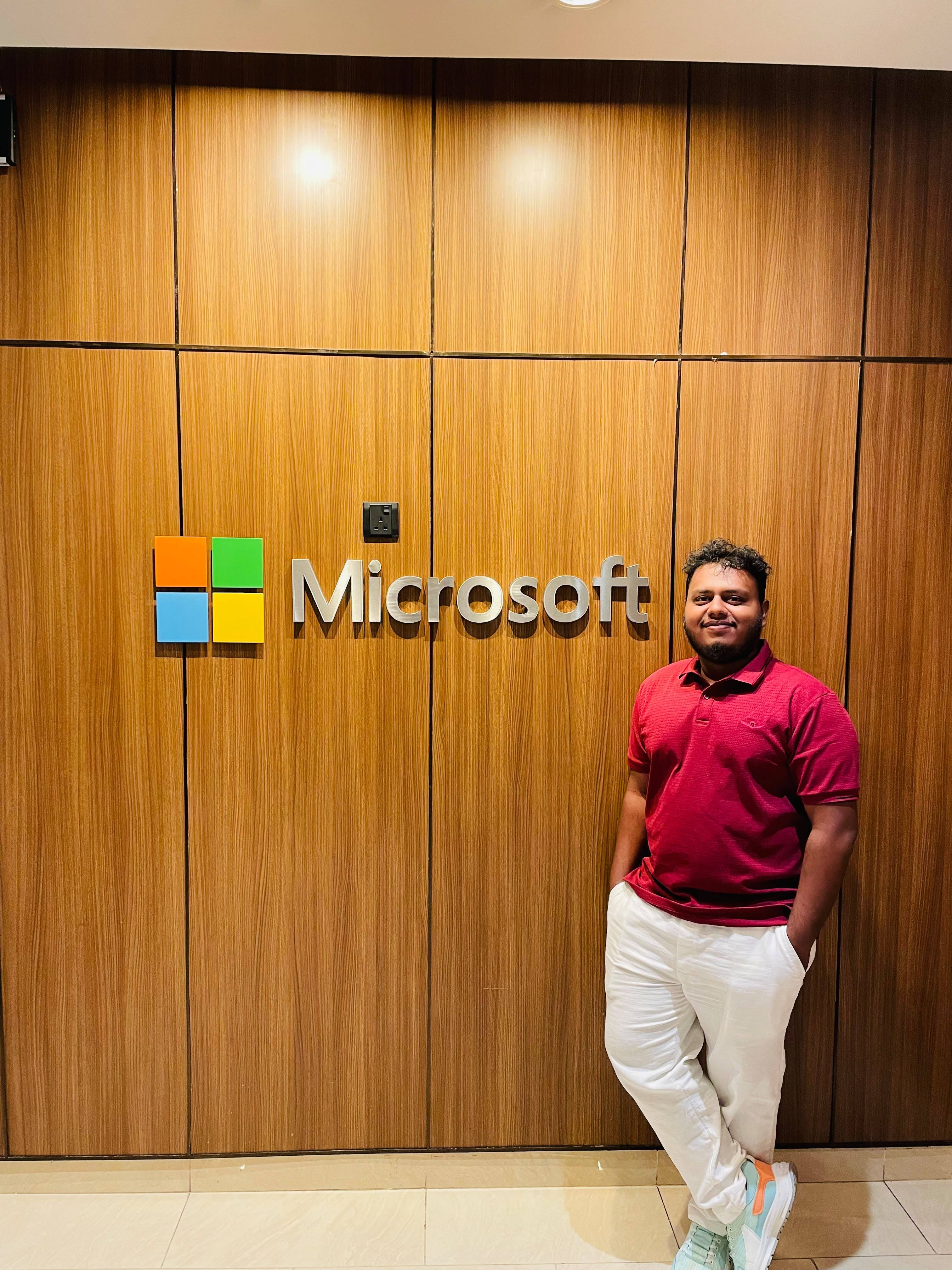 Aweesha Wijesundara standing beside the Microsoft logo on a wood-panelled wall