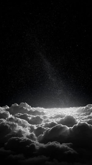 Black star-filled night sky above a horizon of softly illuminated clouds, with a faint Milky Way rising into darkness.